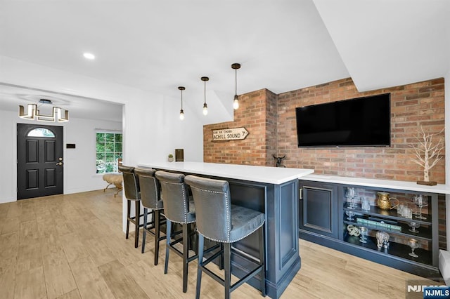 bar featuring brick wall, light wood-style flooring, bar area, and decorative light fixtures