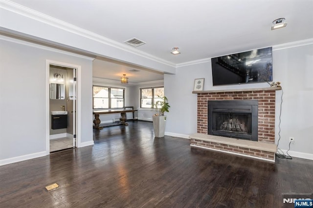 living area featuring wood finished floors, visible vents, baseboards, a brick fireplace, and crown molding