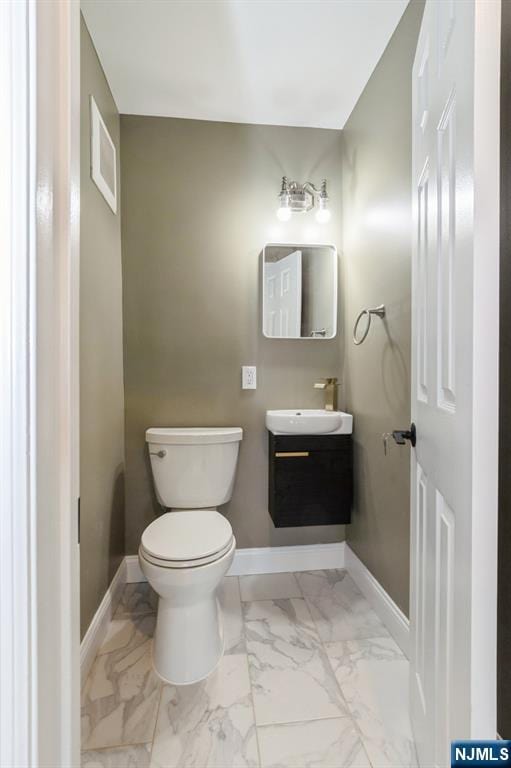 half bathroom featuring toilet, marble finish floor, baseboards, and vanity