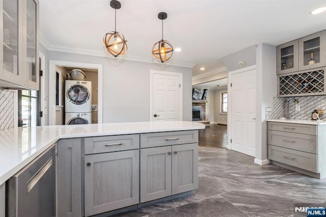 kitchen featuring a peninsula, stacked washing maching and dryer, crown molding, and gray cabinetry