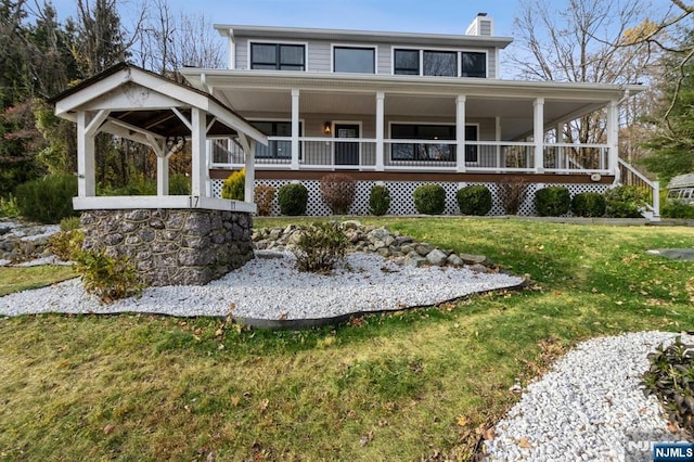 view of front of home with covered porch, a front lawn, and a chimney