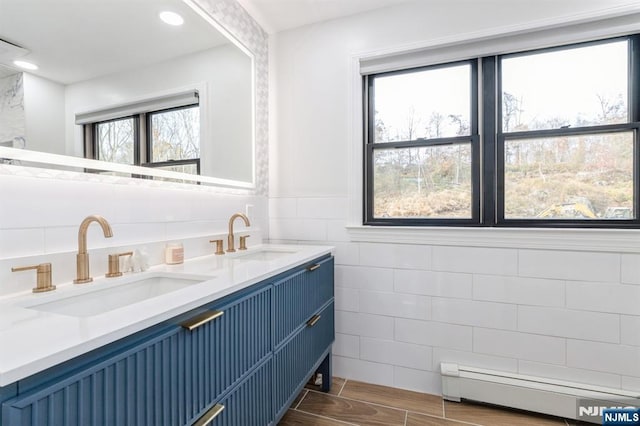 full bath with double vanity, tile walls, baseboard heating, and a sink