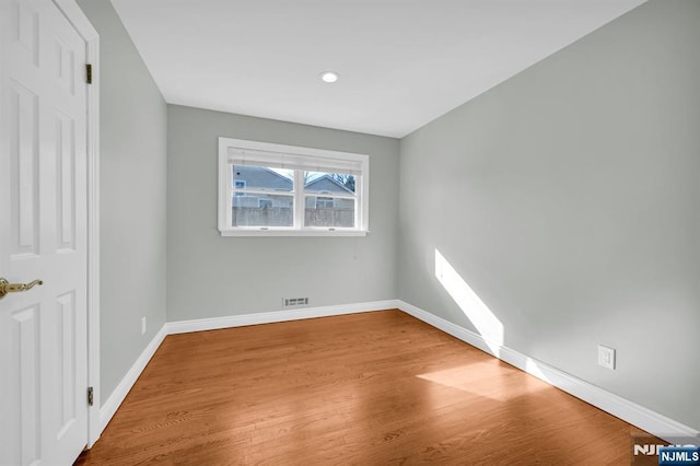 empty room with wood finished floors, visible vents, and baseboards