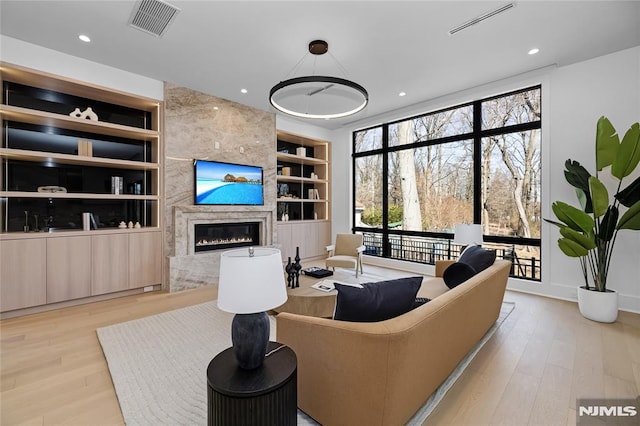 living area featuring built in shelves, recessed lighting, visible vents, a premium fireplace, and wood finished floors