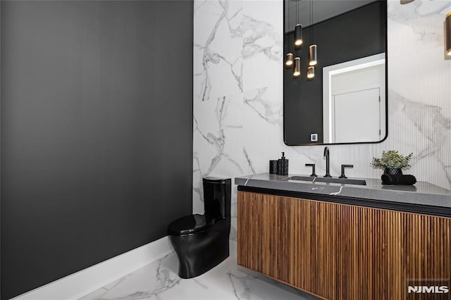 bathroom with toilet, marble finish floor, vanity, and stone wall