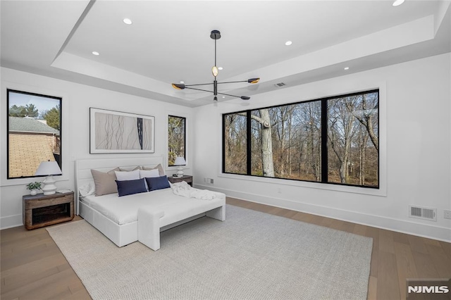 bedroom with a chandelier, a tray ceiling, wood finished floors, and visible vents