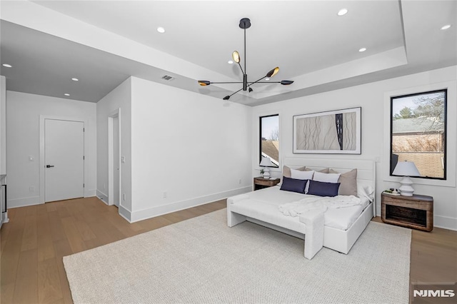 bedroom featuring light wood-type flooring, a tray ceiling, multiple windows, and recessed lighting