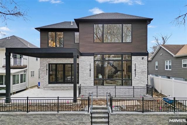 rear view of property featuring a fenced front yard, stone siding, and a patio