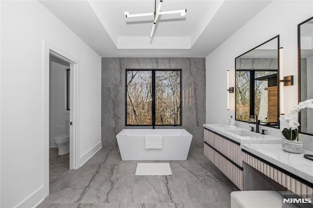 bathroom with marble finish floor, a soaking tub, a raised ceiling, and toilet