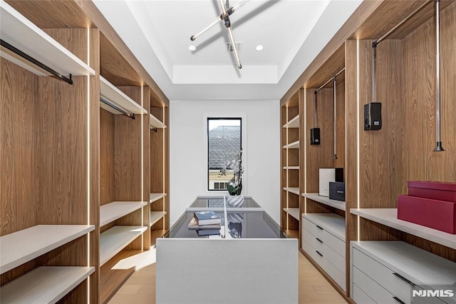 walk in closet featuring light wood-type flooring and a tray ceiling