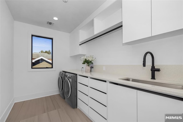 washroom with a sink, visible vents, baseboards, washer and dryer, and cabinet space