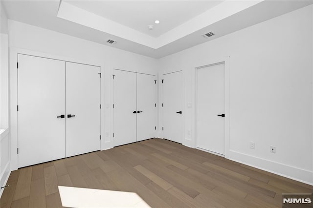 unfurnished bedroom with a tray ceiling, visible vents, multiple closets, and wood finished floors