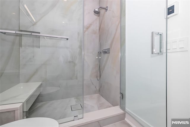 bathroom featuring a marble finish shower and toilet