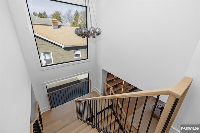 staircase featuring a towering ceiling, a notable chandelier, baseboards, and wood finished floors