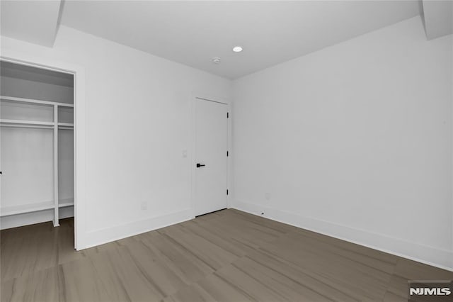 unfurnished bedroom with a spacious closet, recessed lighting, wood finished floors, and baseboards