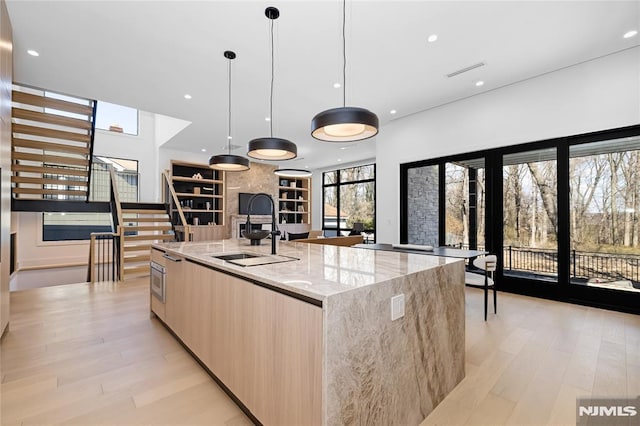 kitchen with light wood-style flooring, light brown cabinetry, open floor plan, a sink, and modern cabinets