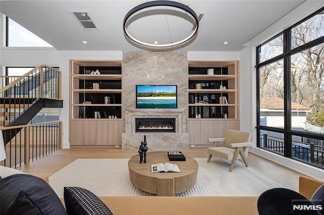 living area featuring built in shelves, recessed lighting, visible vents, a high end fireplace, and wood finished floors