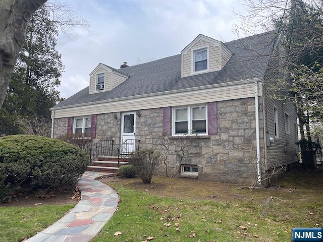 cape cod house featuring stone siding, a chimney, and a front yard