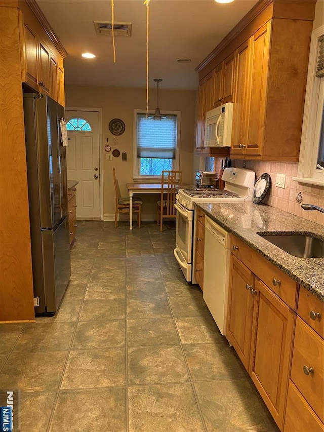 kitchen with white appliances, brown cabinets, light stone countertops, tasteful backsplash, and a sink