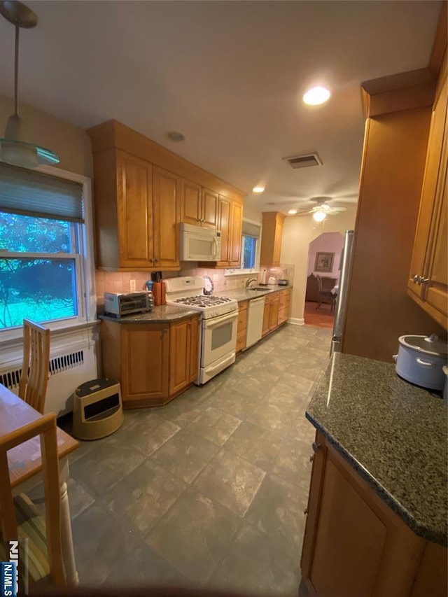 kitchen with white appliances, radiator heating unit, decorative backsplash, ceiling fan, and dark stone countertops