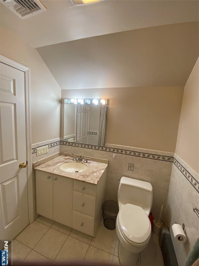 half bathroom with tile walls, a wainscoted wall, tile patterned floors, toilet, and vanity