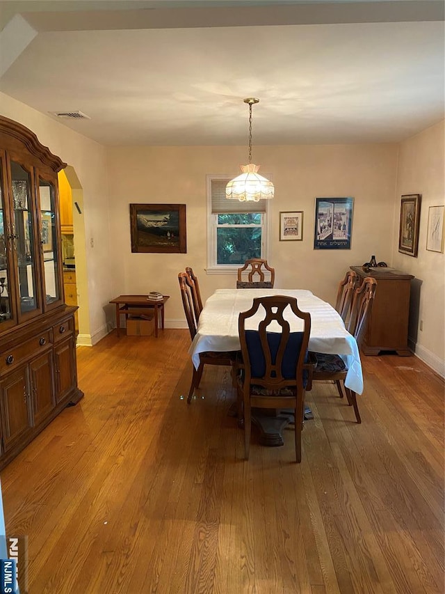 dining space featuring arched walkways, light wood-style flooring, and baseboards