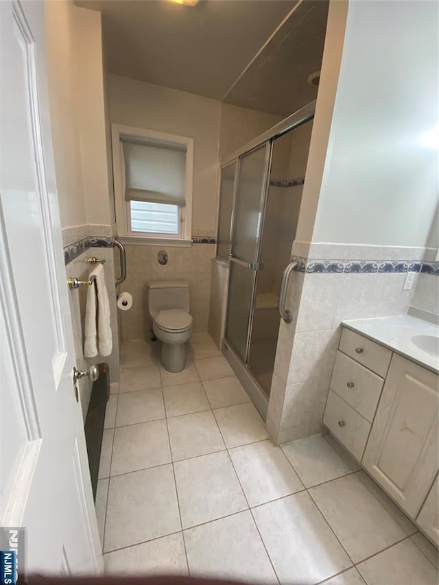bathroom featuring tile walls, tile patterned floors, wainscoting, a stall shower, and toilet