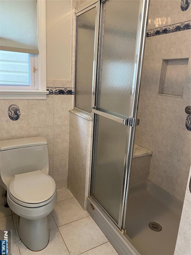 bathroom featuring a shower stall, tile patterned floors, toilet, and tile walls