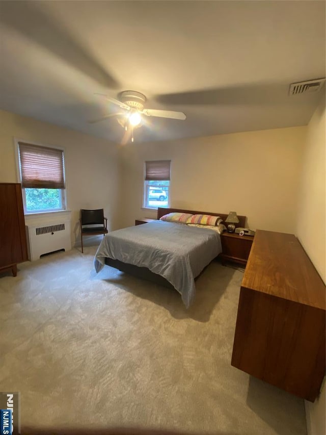 bedroom with radiator, multiple windows, light carpet, and ceiling fan