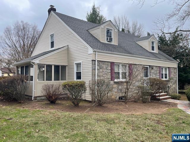 view of front of house featuring a front yard, a chimney, stone siding, a shingled roof, and a sunroom