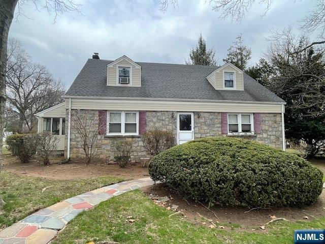 new england style home with stone siding, a chimney, a front lawn, and roof with shingles