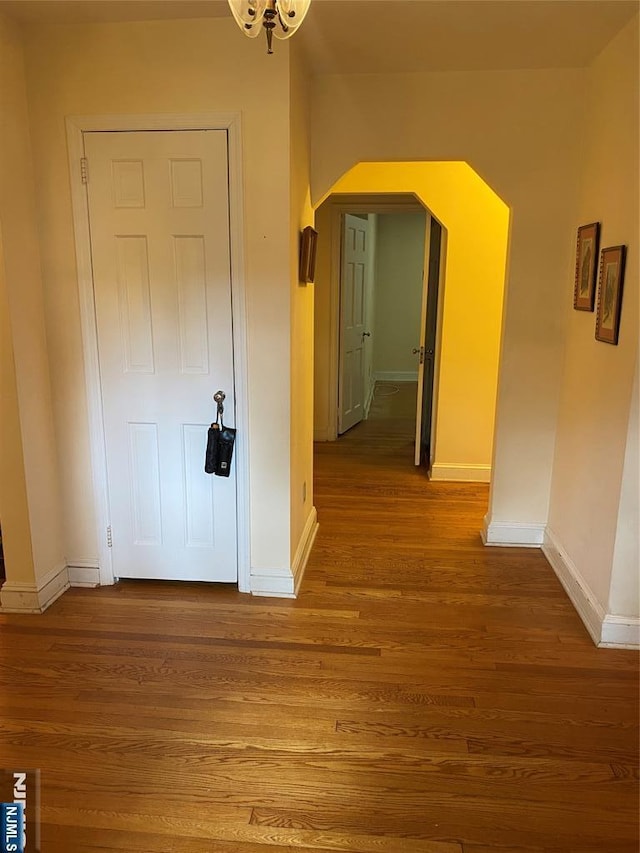 hallway with arched walkways, baseboards, and wood finished floors