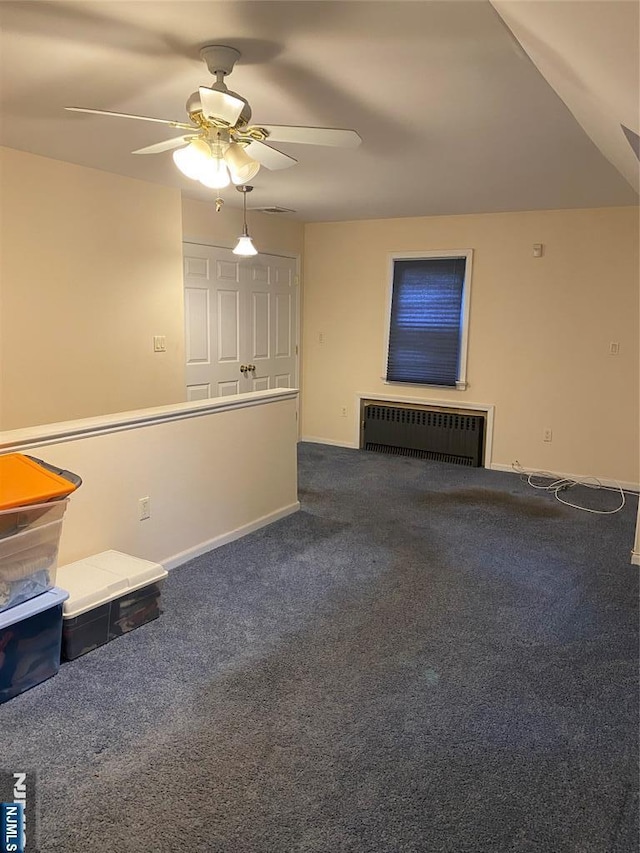 unfurnished living room with radiator heating unit, a ceiling fan, baseboards, and dark colored carpet
