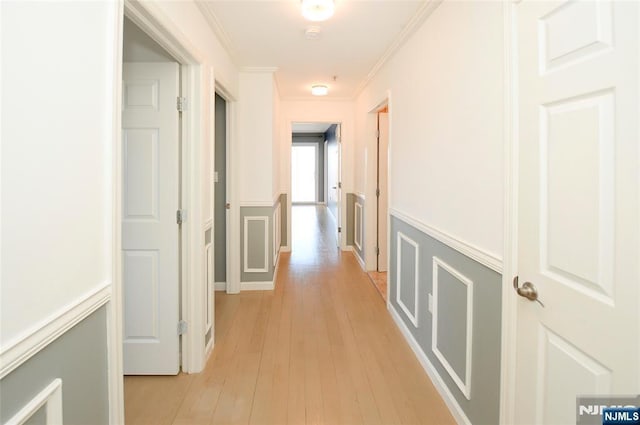 hallway with crown molding, wainscoting, a decorative wall, and light wood-style flooring