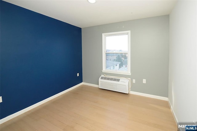 unfurnished room featuring baseboards, a wall mounted AC, and light wood-style floors