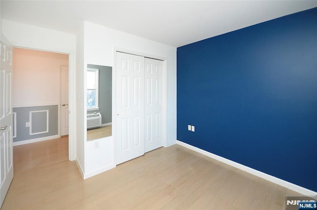 unfurnished bedroom featuring a wall unit AC, light wood finished floors, baseboards, and a closet