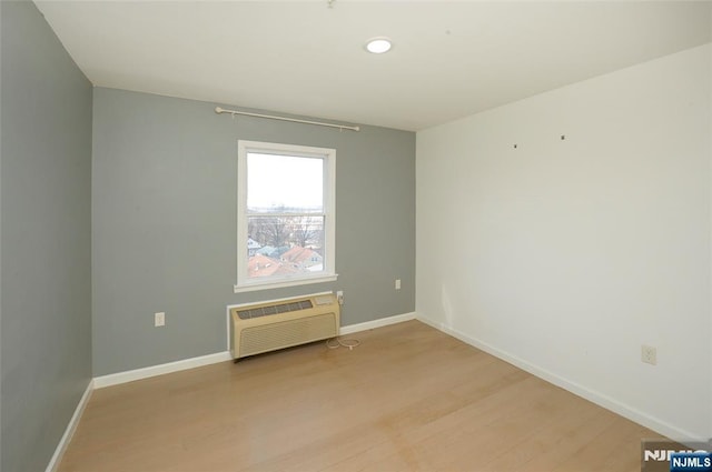 unfurnished room with light wood-style floors, an AC wall unit, and baseboards