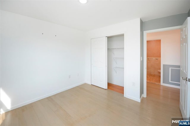 unfurnished bedroom featuring light wood-style flooring, baseboards, and a closet