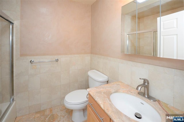 full bathroom with enclosed tub / shower combo, toilet, a wainscoted wall, vanity, and tile walls