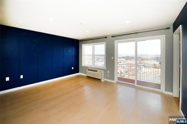 unfurnished room with an AC wall unit, recessed lighting, wood finished floors, and baseboards