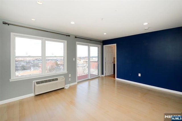 unfurnished room with recessed lighting, light wood-style flooring, baseboards, and a wall mounted AC