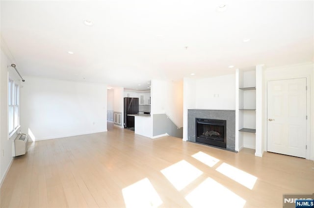 unfurnished living room with a fireplace, recessed lighting, ornamental molding, light wood-type flooring, and baseboards