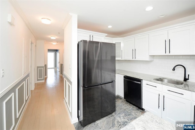 kitchen featuring black dishwasher, white cabinets, freestanding refrigerator, light stone countertops, and a sink