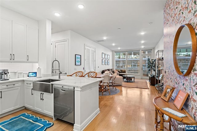 kitchen featuring light wood-style flooring, open floor plan, a peninsula, stainless steel dishwasher, and a sink