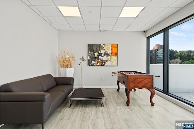 recreation room featuring a paneled ceiling, baseboards, a city view, and wood finished floors