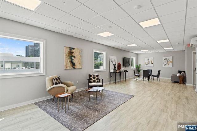 living area featuring a drop ceiling, plenty of natural light, wood finished floors, and baseboards