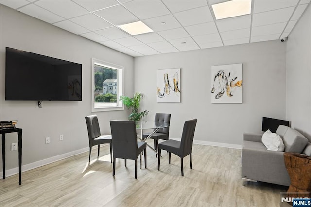 dining area featuring a paneled ceiling, light wood finished floors, and baseboards