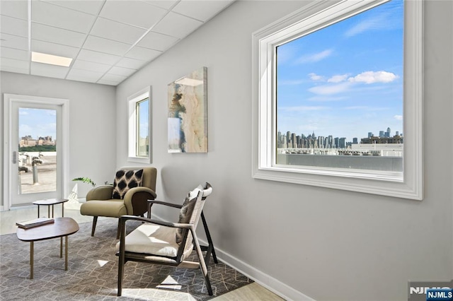 living area with a view of city, a drop ceiling, baseboards, and wood finished floors