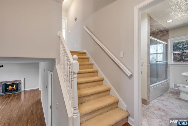 stairway with wood finished floors, a fireplace, baseboards, and a textured ceiling