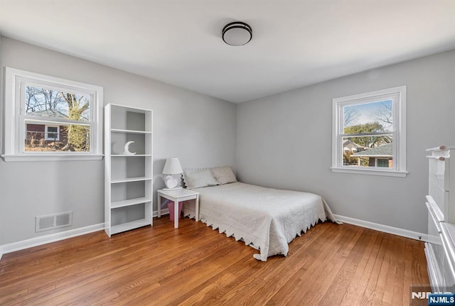 bedroom with visible vents, multiple windows, light wood-style flooring, and baseboards